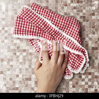 Hands hold white red checkered kitchen towel on a brown background, top view Stock Photo