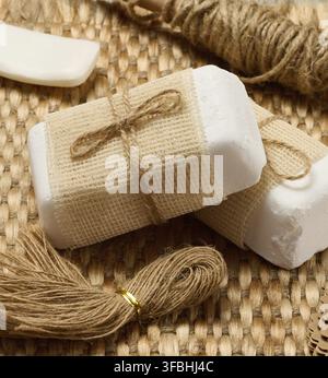 Natural handmade soap bars with various craft supplies on a woven mat. The soap bars are wrapped in burlap and twine Stock Photo