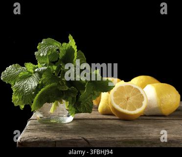 Yellow ripe lemon and a bunch of fresh green mint on a wooden board, ingredients for lemonade, black background Stock Photo