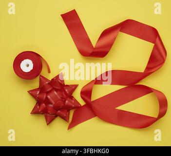 Bow and twisted silk red ribbon on a yellow background, top view Stock Photo