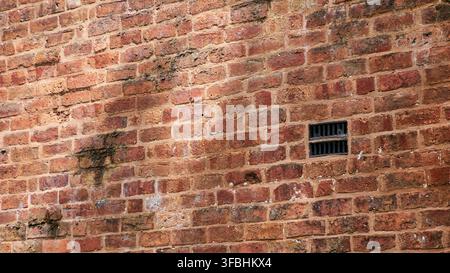 a redbrick wall with vent and shadows, full frame. Stock Photo