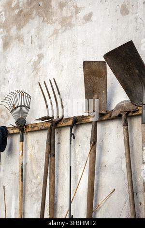 A collection of various used rusty garden tools hanging on white wall Stock Photo
