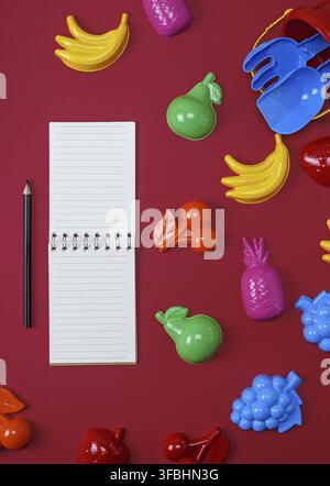 Open notebook with empty white sheets and black wooden pencils on a red background, top view Stock Photo