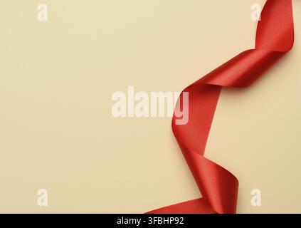 Curled red silk ribbon on a beige background, copy space Stock Photo
