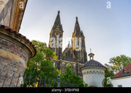 The Basilica of St. Peter and Paul stands tall in Vysehrad. Bright sunlight shines from behind the church, highlighting its towers and stone details. The area is quiet and open. Stock Photo