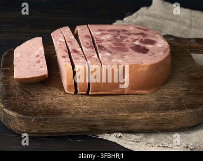 Sliced boiled sausage with slices of whole meat on a brown wooden cutting board, close up Stock Photo
