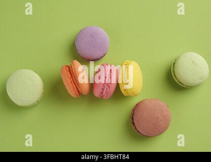 Baked multi-colored macaroon cookies lie in a row on a green background, top view Stock Photo