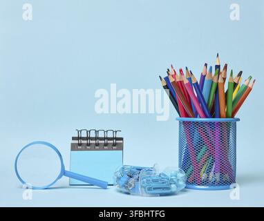 Set of office supplies including colored pencils in a glass, magnifying glass, notepad and paper clips symbolizing learning, organization or creativit Stock Photo