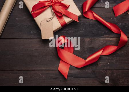 Roll of brown kraft packaging paper, red silk ribbon on a brown wooden background, top view Stock Photo