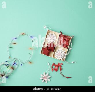 Burning christmas garland on a white wire with colorful lights and box with wooden toys for the Christmas tree on a green background Stock Photo