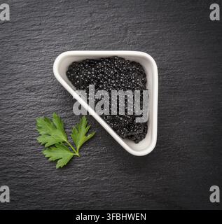 Black grainy caviar of paddlefish fish in a white ceramic bowl, black background, top view Stock Photo