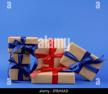 Rectangle box wrapped in brown kraft paper and tied with a silk blue and red ribbon, gift on a dark blue background, holiday backdrop Stock Photo