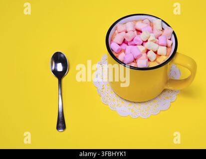 Yellow cup with multi-colored marshmallow slices on a yellow background, top view Stock Photo