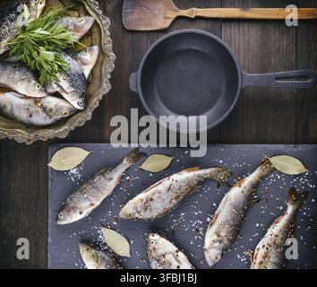 River fish on a black board and a black cast-iron frying pan on a brown table, top view Stock Photo