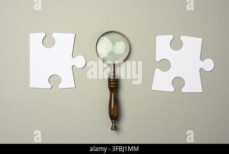 Puzzles around a magnifying glass on a gray background. concept of searching for talented people, recruiting personnel, finding a solution to the prob Stock Photo