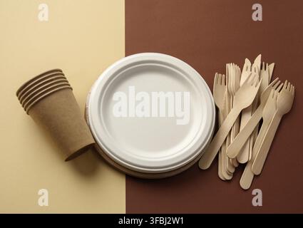 Paper cup and wooden fork, empty round brown disposable plate made from recycled materials on a brown background. Concept of the absence of non-recycl Stock Photo