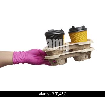 Hand in a pink latex glove holds a paper tray with disposable cardboard cups and plastic covers on a white background, safe and contactless delivery o Stock Photo