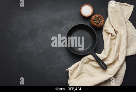 Empty black round cast iron frying pan with handle on black table, top view. Copy space Stock Photo