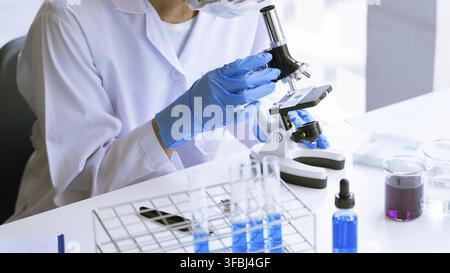 Young Asian scientist Working looking through a microscope doing research for analyzing a Experiments sample in a forensic laboratory Stock Photo