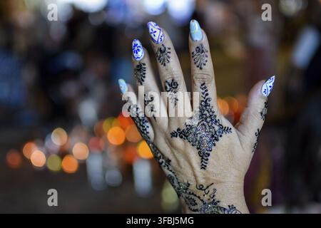 Hands showing painting henna tattoo with background of colorful lights at night. Marrakech Stock Photo