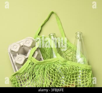 Reusable green textile shopping bag with empty bottles and egg cartons on a green background, zero waste Stock Photo