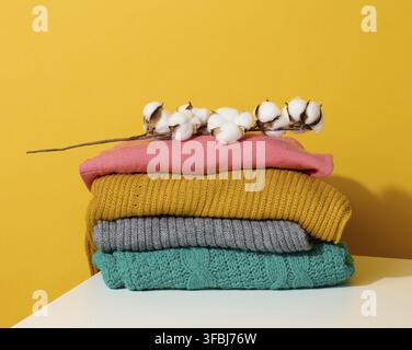 Stack of folded knitted sweaters on yellow background. Comfortable clothes, wash Stock Photo