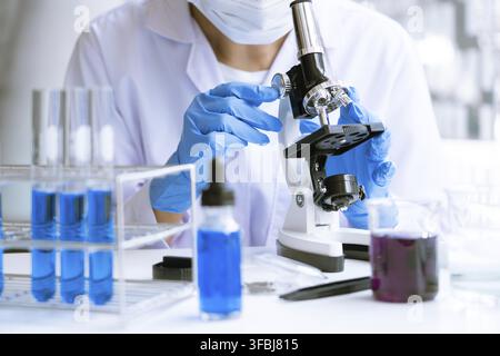 Young Asian scientist Working looking through a microscope doing research for analyzing a Experiments sample in a forensic laboratory Stock Photo