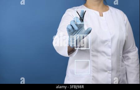 Woman doctor in a white medical coat, blue latex gloves stands on a blue background, hand touches and notes in the list on a virtual screen Stock Photo