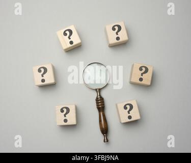 Wooden magnifier and cubes with question marks on gray background. ?oncept of finding an answer to questions, truth and uncertainty. Answers on questi Stock Photo