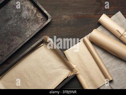 Empty rectangular metal pan covered with brown parchment paper and paper rolls on a wooden table, top view Stock Photo