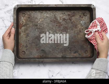 Hand hold empty metal rectangular baking sheet on a white table, top view Stock Photo