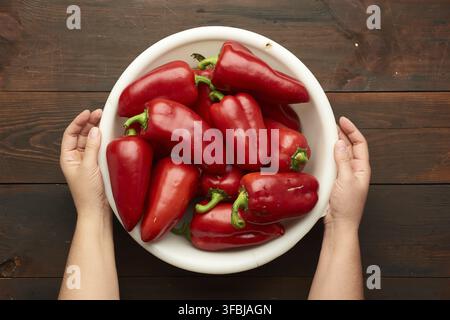Female hands holding a large white plastic bowl with red pepper, top view Stock Photo