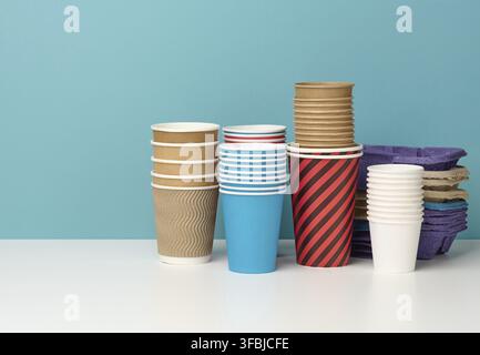 Stack of paper disposable multi-colored cups and stand on white table, blue background Stock Photo