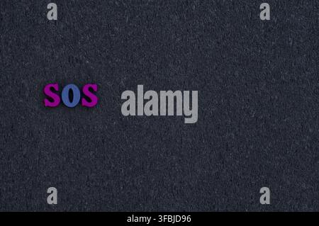 Wooden letters on the black surface, empty space on the right, the word sos Stock Photo