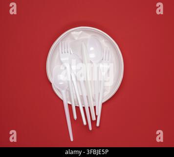 Round plate and stack of plastic forks and spoons on red background, top view Stock Photo
