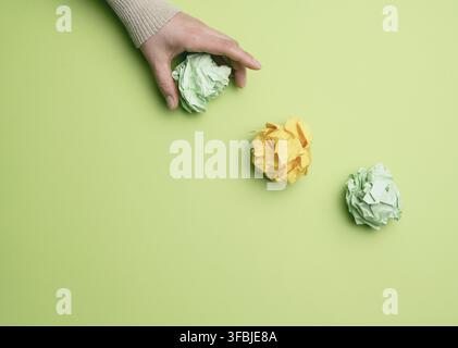 Three crumpled balls of colored paper on a green background, hand throws paper Stock Photo