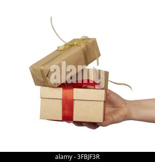 Hand holds a stack of wrapped gifts in brown craft paper with tied silk bows, subject is isolated on a white background Stock Photo
