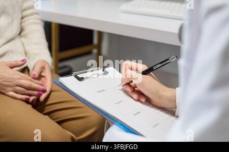 Doctor taking notes during consultation with senior patient in modern clinic Stock Photo