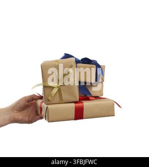 Hand holds a stack of wrapped gifts in brown craft paper with tied silk bows, subject is isolated on a white background Stock Photo