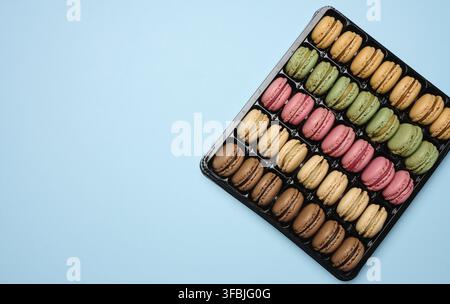 Multi-colored macarons on a blue background in a plastic box, top view. Copy space Stock Photo