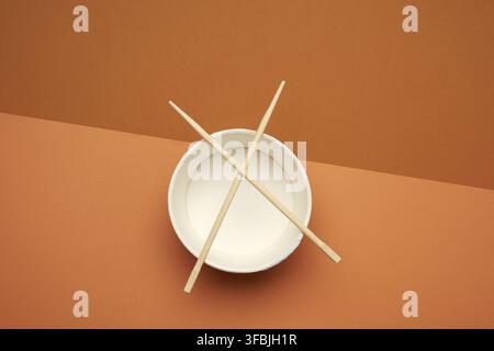 Open empty noodle bowl and pair of wooden sticks on brown background, top view Stock Photo