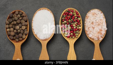 Horizontal row of wooden spoons with black pepper, salt, mixed peppers and pink salt, top view Stock Photo