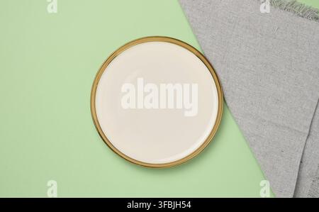 Round ceramic empty white plate and gray linen kitchen towel on green background, top view Stock Photo