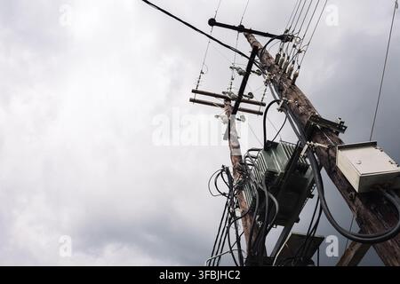 Wooden utility poles carrying heavy electric cables and transformers against a cloudy overcast sky. Stock Photo