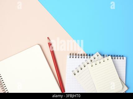Red wooden pencil and stack of spiral open notebooks with blank white sheets on a blue background, top view Stock Photo