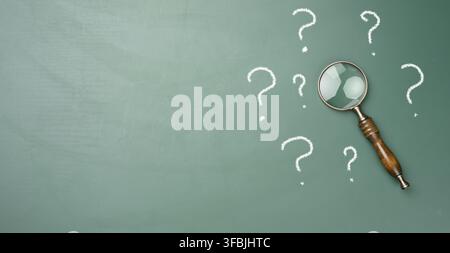 Wooden magnifying glass and white chalk drawn question marks on a green chalk board. The concept of finding solutions, true or false. Answers on quest Stock Photo