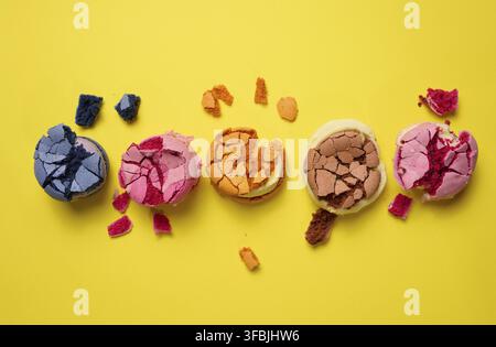 Broken round macarons with crumbs on a yellow background, delicious dessert, top view Stock Photo