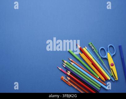Plastic scissors and multicolored wooden pencils on a blue background, flat lay, copy space Stock Photo