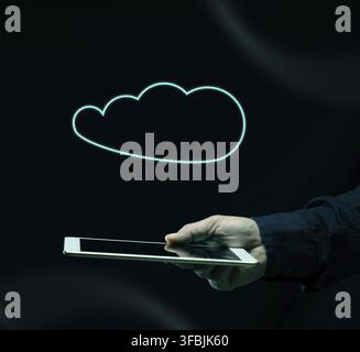 Hand holds a white tablet with a neon cloud outline glowing above it. Concept of cloud computing, data storage, and digitalization on a black backgrou Stock Photo