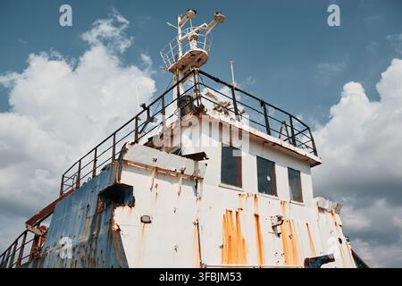 Low angle view of the weathered superstructure and bridge of an abandoned rusty shipwreck under a partly cloudy sky, Greece. Stock Photo